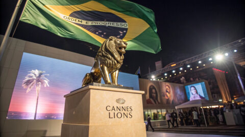 Brazilian flag waving behind golden Cannes Lions trophy statue with creative work displayed in background